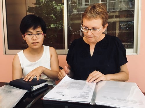 Bà Agnès Munier-Michel (phải) ngồi tại ban công khách sạn ở quận Tân Bình hôm 2/8 lật giở tập hồ sơ điều trị bệnh não úng thủy của con gái Tường Vy Munier-Michel. Ảnh: Hạnh Phạm.